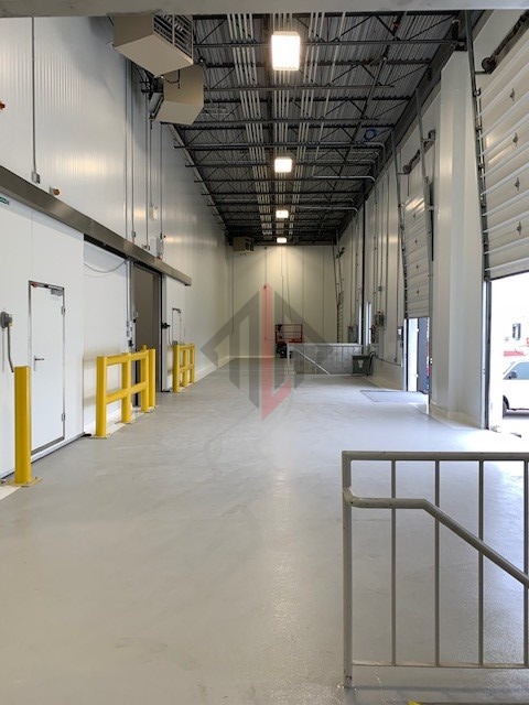 Empty warehouse interior with open loading dock doors and safety barriers.
